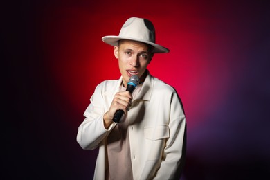 Photo of Talented young man singing on dark background with red light