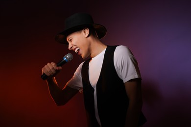 Talented young man singing on dark background with color light