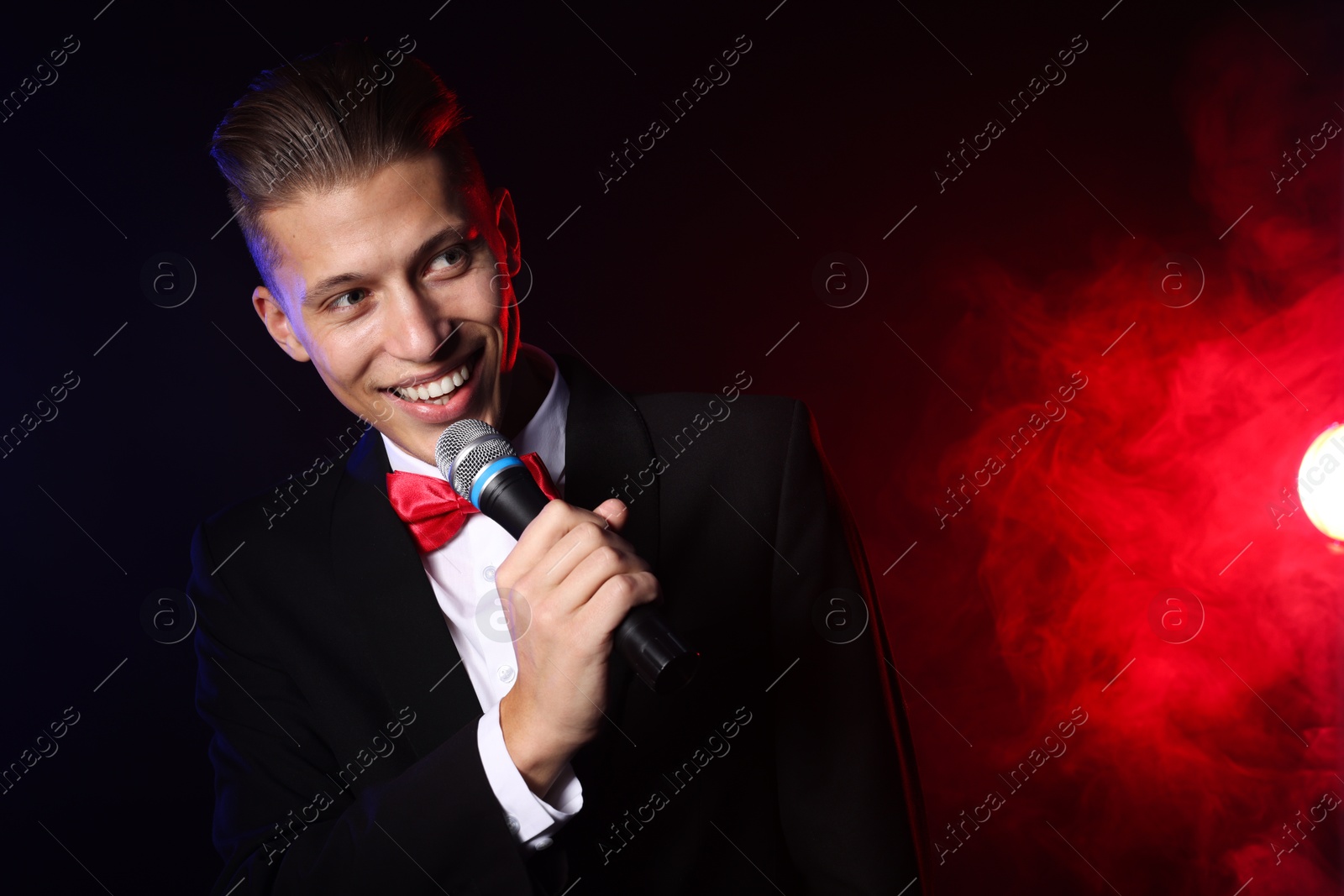 Photo of Talented singer performing on dark background with color lights and smoke. Space for text