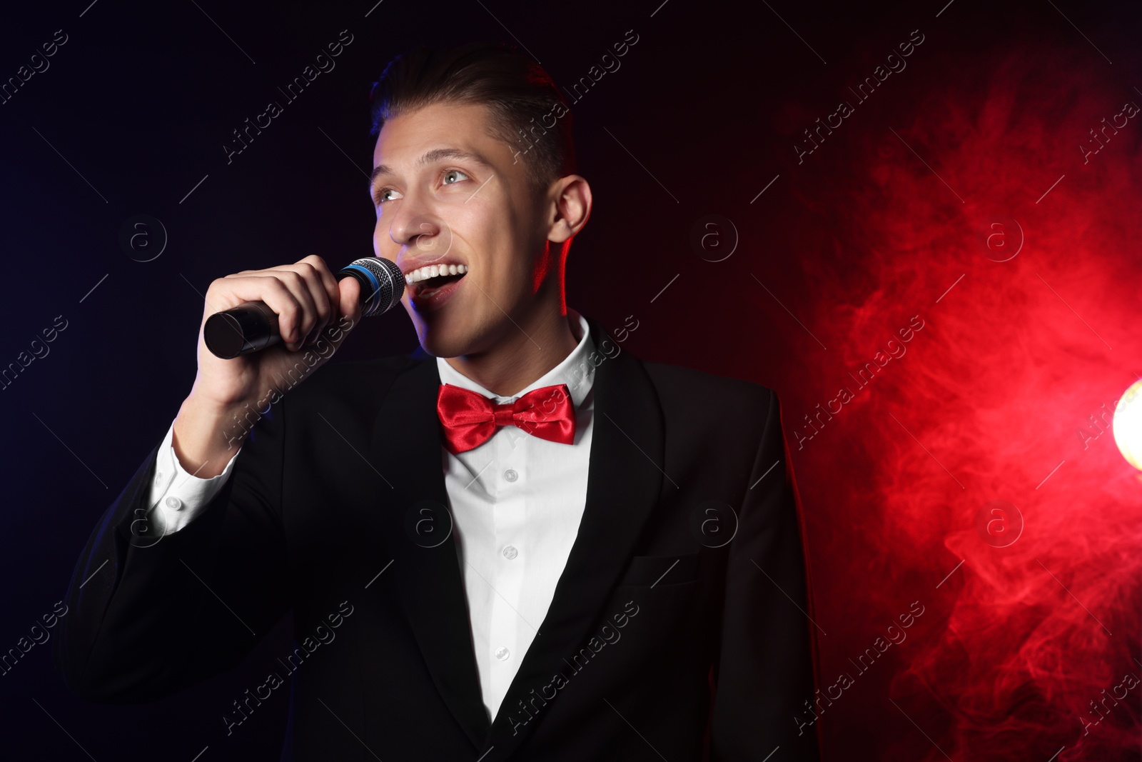 Photo of Talented singer performing on dark background with color lights and smoke. Space for text