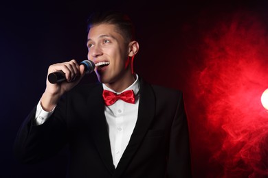 Talented singer performing on dark background with color lights and smoke. Space for text