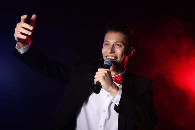 Photo of Talented singer performing on dark background with color lights and smoke