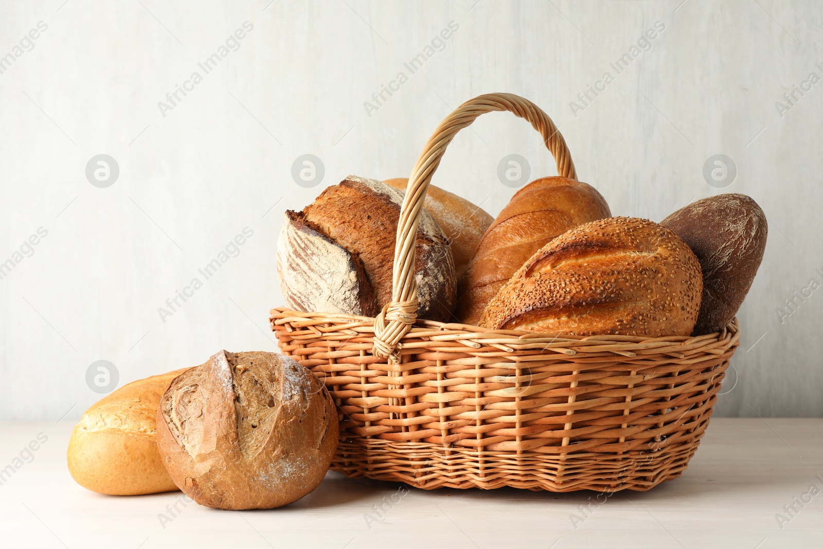 Photo of Different freshly baked bread loafs and wicker basket on white wooden table