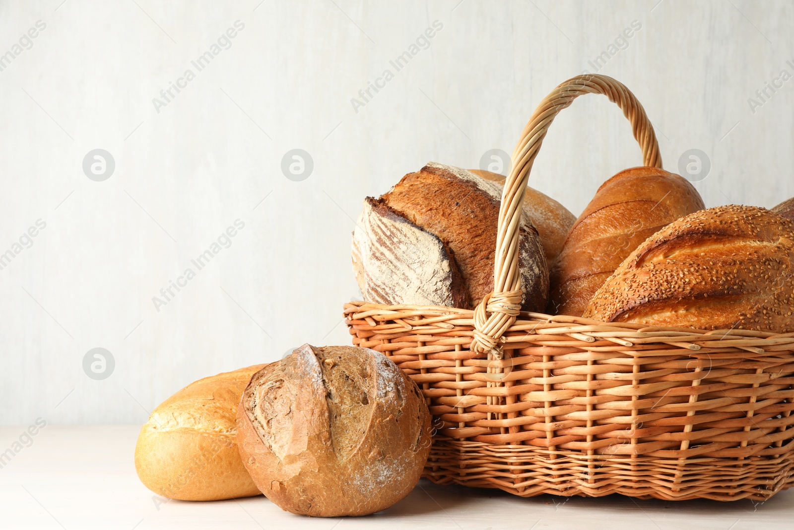 Photo of Different freshly baked bread loafs and wicker basket on white wooden table, closeup. Space for text