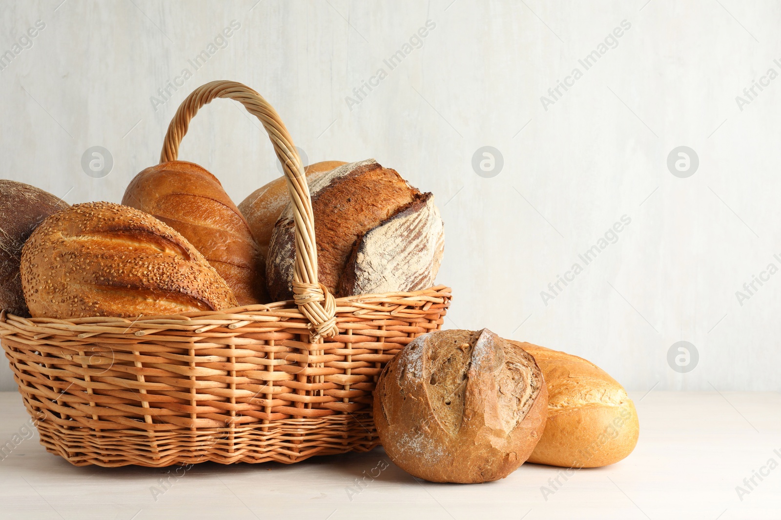 Photo of Different freshly baked bread loafs and wicker basket on white wooden table, closeup. Space for text