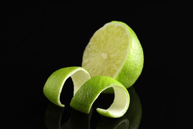 Photo of Lime peel and half of fresh fruit on black mirror surface, closeup