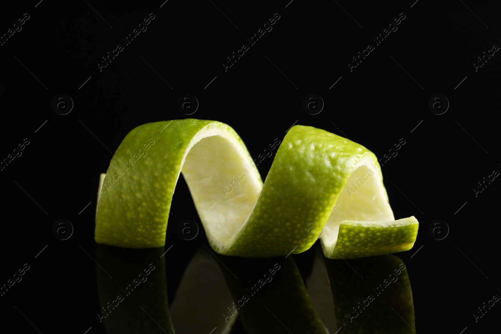 Photo of One curly lime peel on black mirror surface, closeup