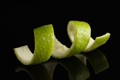 Photo of One curly lime peel on black mirror surface, closeup