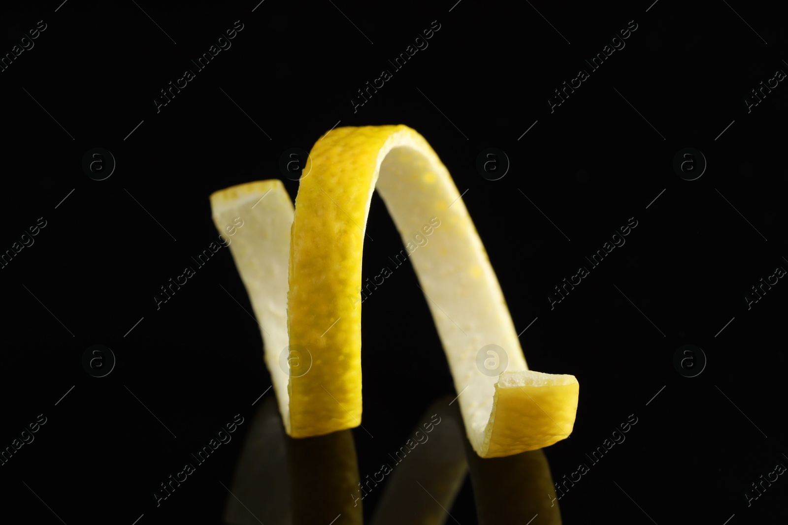 Photo of One curly lemon peel on black mirror surface, closeup