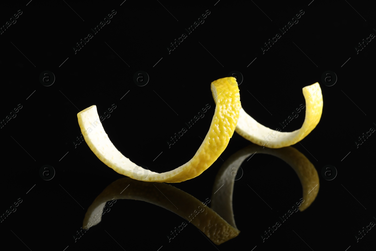 Photo of One curly lemon peel on black mirror surface, closeup