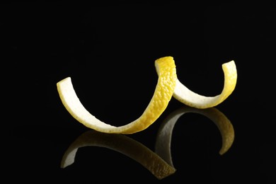 Photo of One curly lemon peel on black mirror surface, closeup