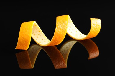 Photo of One curly orange peel on black mirror surface, closeup