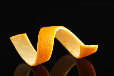 Photo of One curly orange peel on black mirror surface, closeup