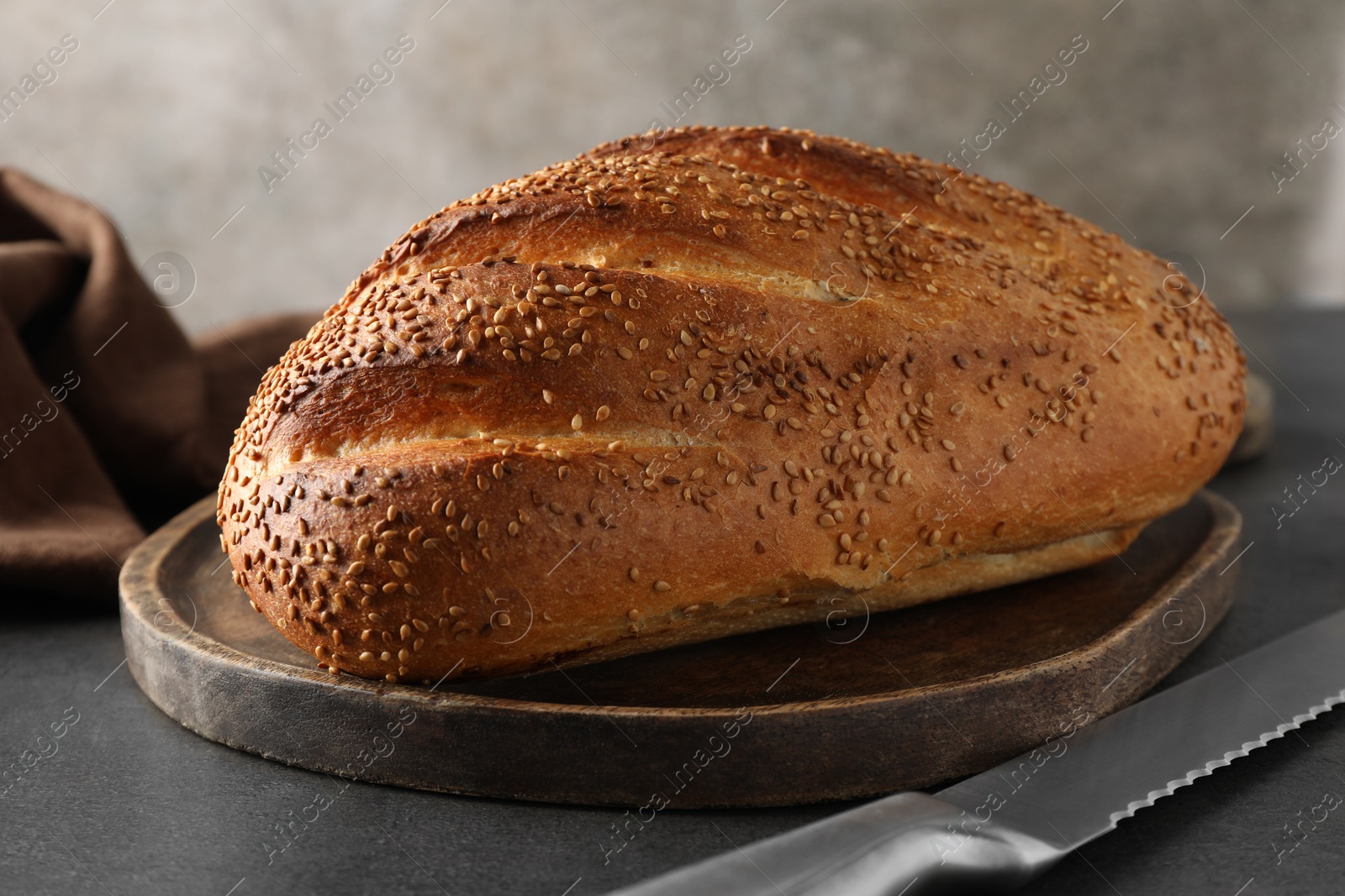 Photo of Freshly baked bread with seeds and knife on grey table, closeup