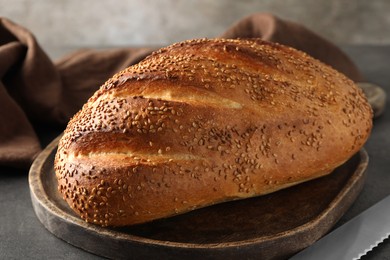 Photo of Freshly baked bread with seeds and knife on grey table, closeup