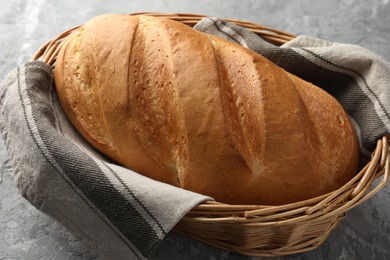 Photo of Freshly baked bread in wicker basket on grey table, closeup