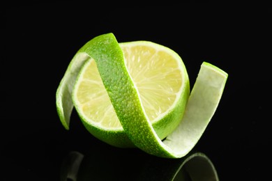 Photo of Fresh lime peel and half of fruit on black glass surface, closeup