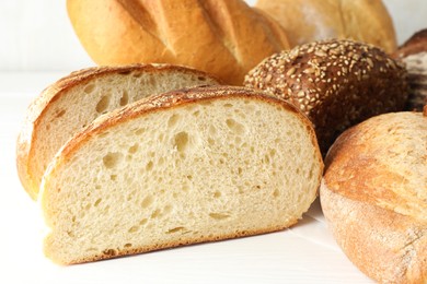 Photo of Whole and cut bread loafs on white table, closeup