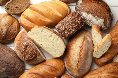 Photo of Whole and cut bread loafs on white wooden table, flat lay