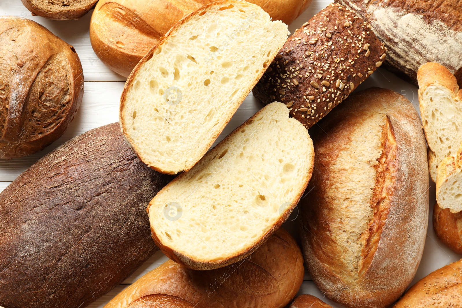 Photo of Whole and cut bread loafs on white wooden table, flat lay