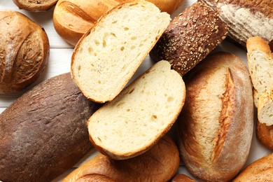 Photo of Whole and cut bread loafs on white wooden table, flat lay