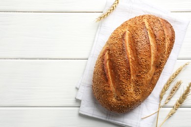 Photo of Loaf of bread with sesame seeds and spikes on white wooden table, flat lay. Space for text