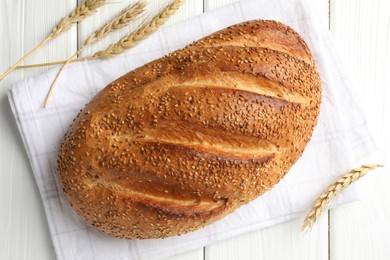 Photo of Loaf of bread with sesame seeds and spikes on white wooden table, flat lay