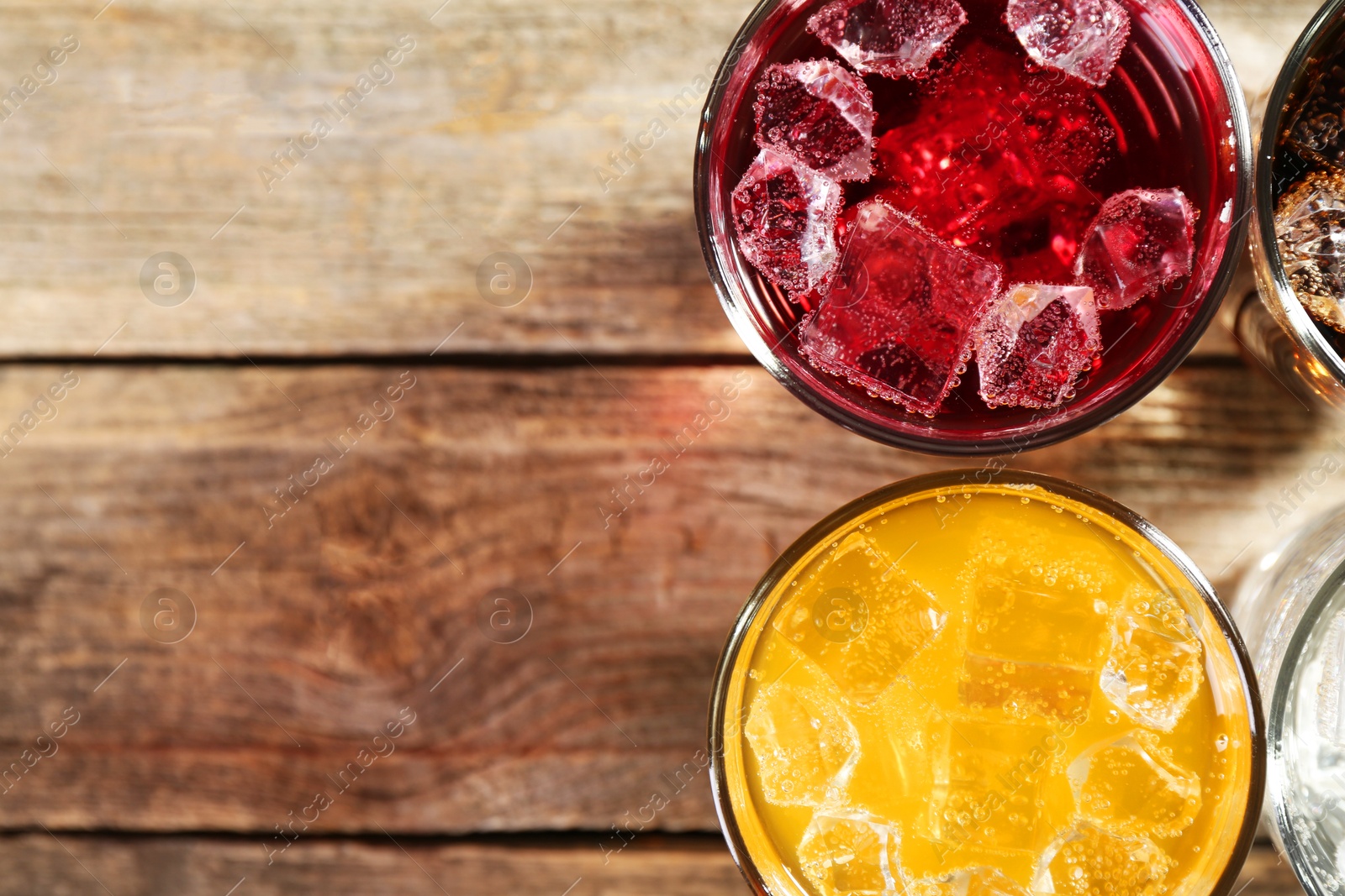 Photo of Soda water of different flavors with ice cubes in glasses on wooden table, top view. Space for text