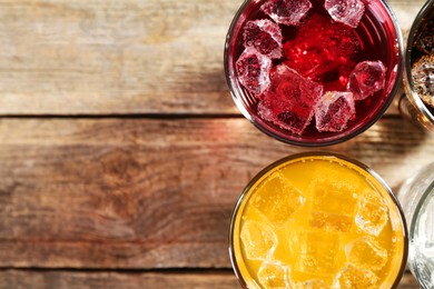 Photo of Soda water of different flavors with ice cubes in glasses on wooden table, top view. Space for text