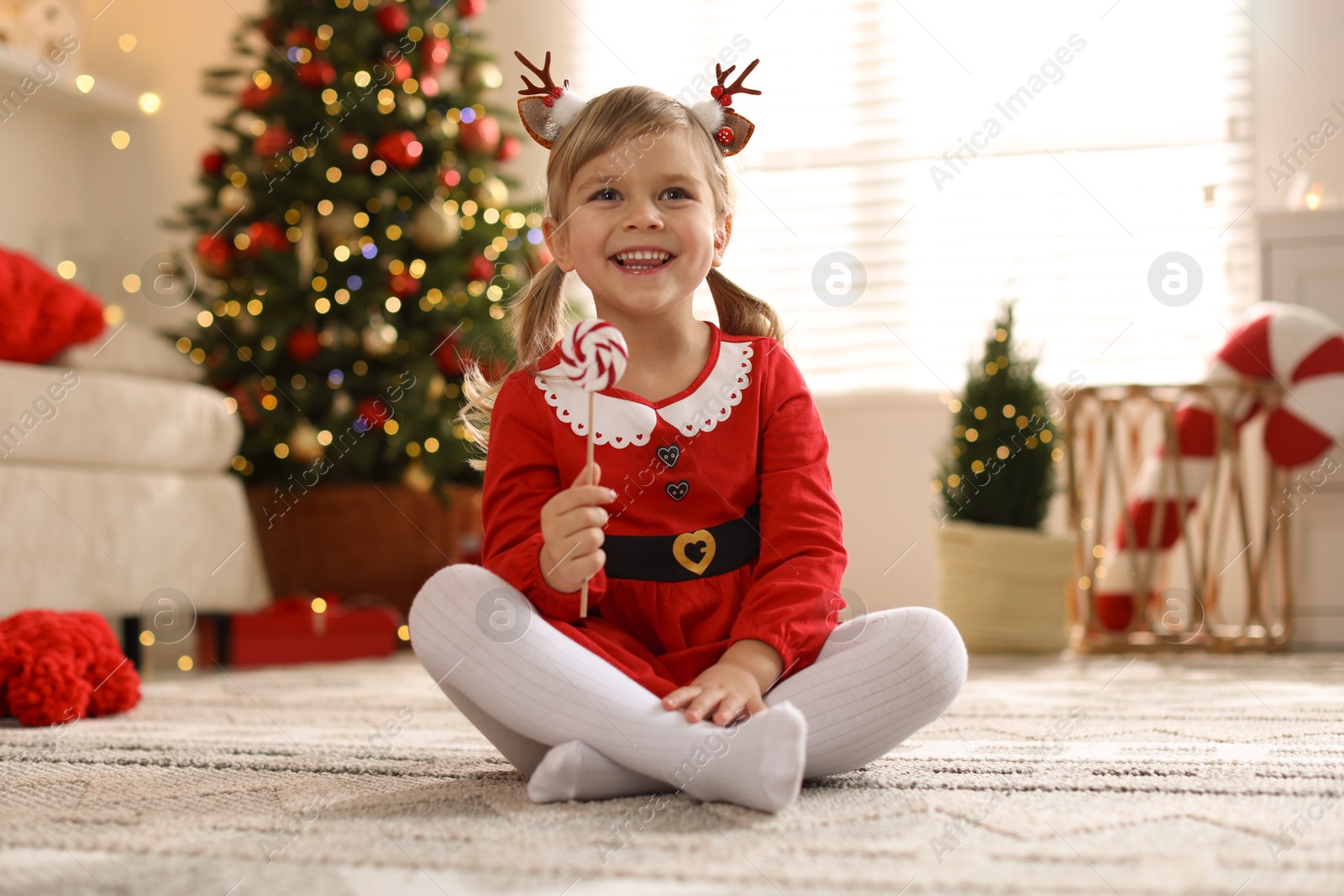 Photo of Little girl in Christmas costume with lollipop at home