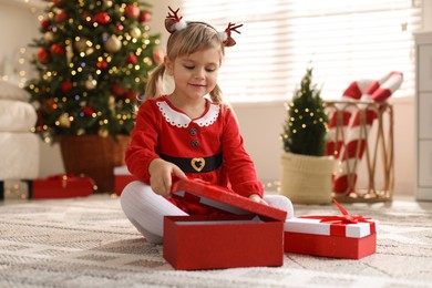 Photo of Little girl in Christmas costume with gift boxes at home