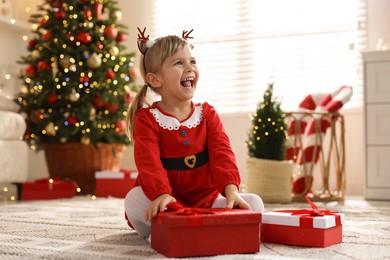 Photo of Little girl in Christmas costume with gift boxes at home