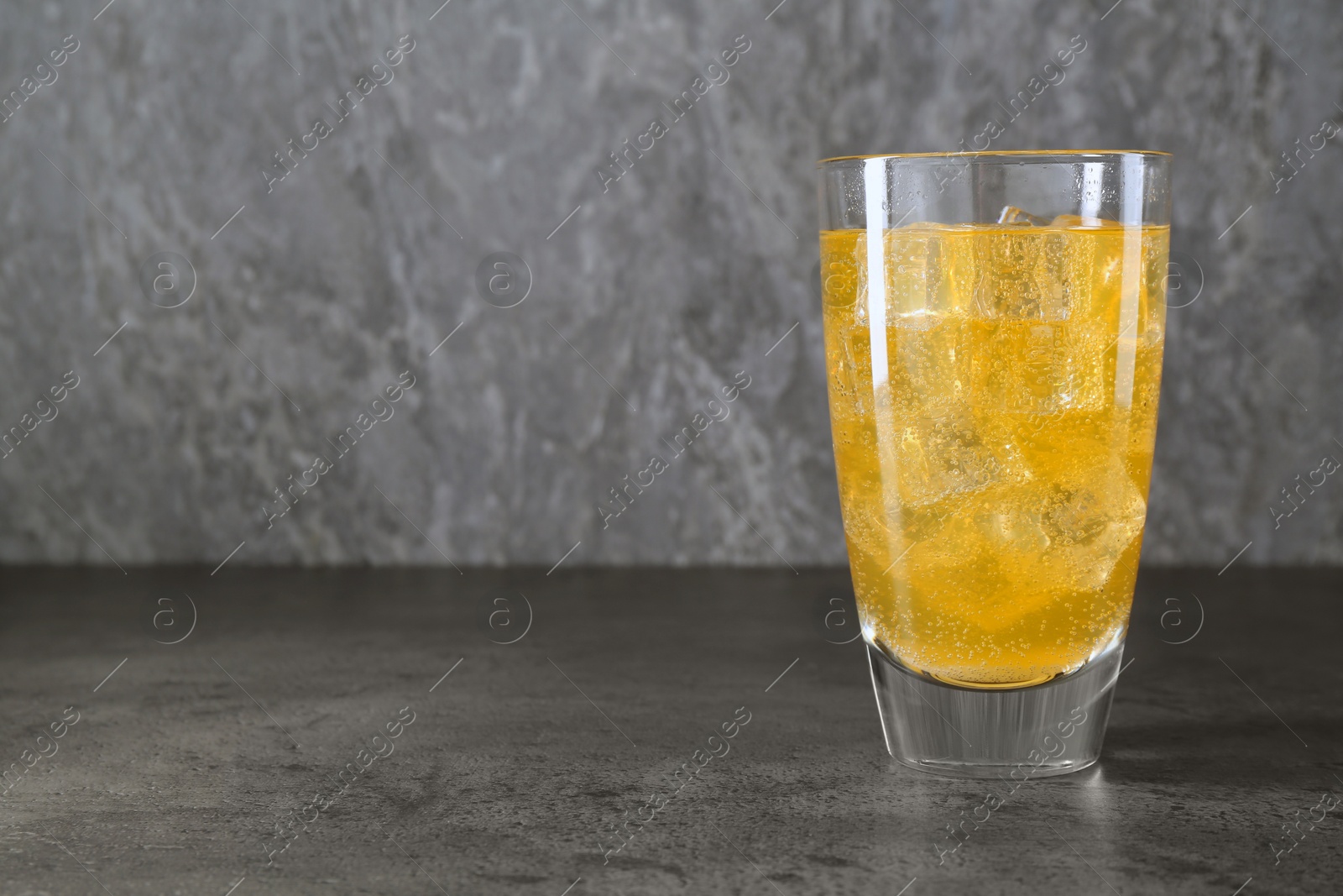 Photo of Sweet soda water with ice cubes in glass on grey table, space for text