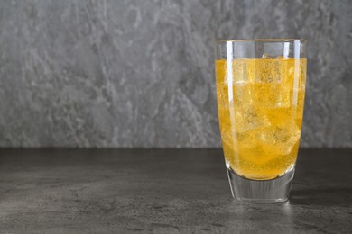 Photo of Sweet soda water with ice cubes in glass on grey table, space for text