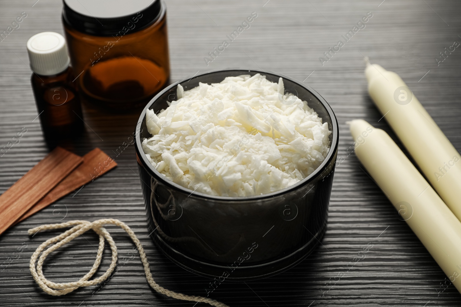 Photo of Soy wax, essential oil, twine, jar, wooden wicks and candles on black textured table, closeup