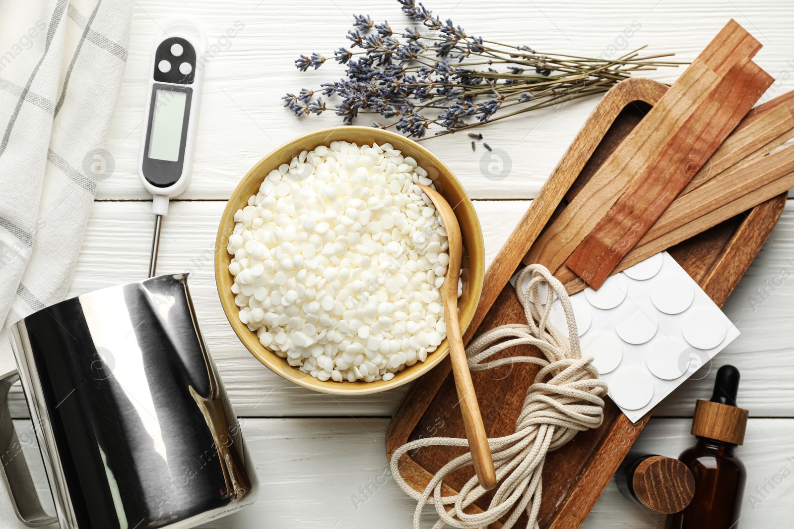 Photo of Soy wax in bowl, essential oils and different tools for making candles on white wooden table, flat lay