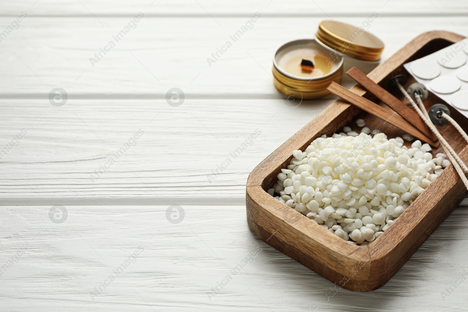 Photo of Soy wax, wicks, sticker and candle on white wooden table, closeup. Space for text