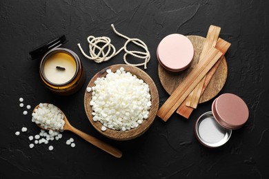 Photo of Soy wax in bowl, candle, wooden wicks, twine and jars on black table, flat lay