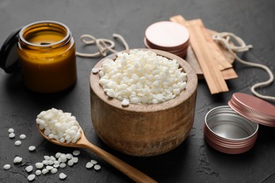 Photo of Soy wax in bowl, candle, wooden wicks, twine and jars on black table, closeup