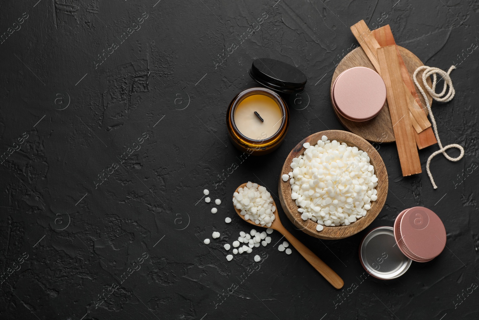 Photo of Soy wax in bowl, candle, wooden wicks, twine and jars on black table, flat lay. Space for text