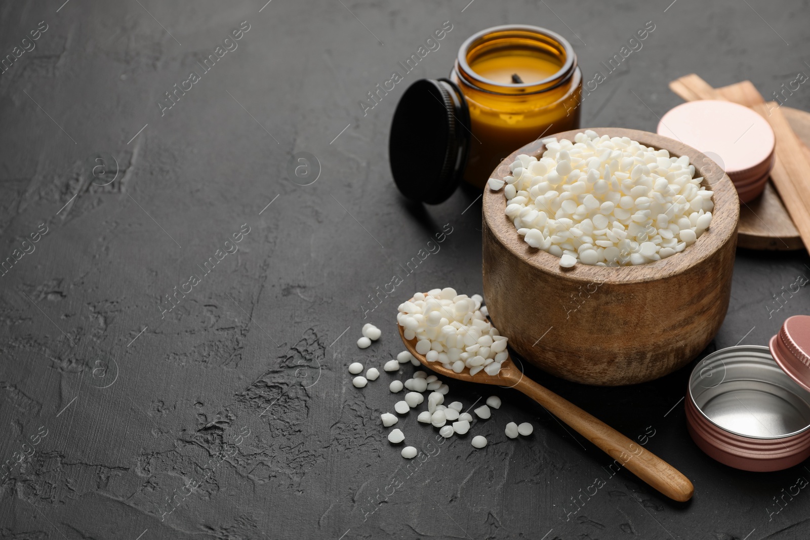 Photo of Soy wax in bowl, candle, wooden wicks and jars on black table, space for text