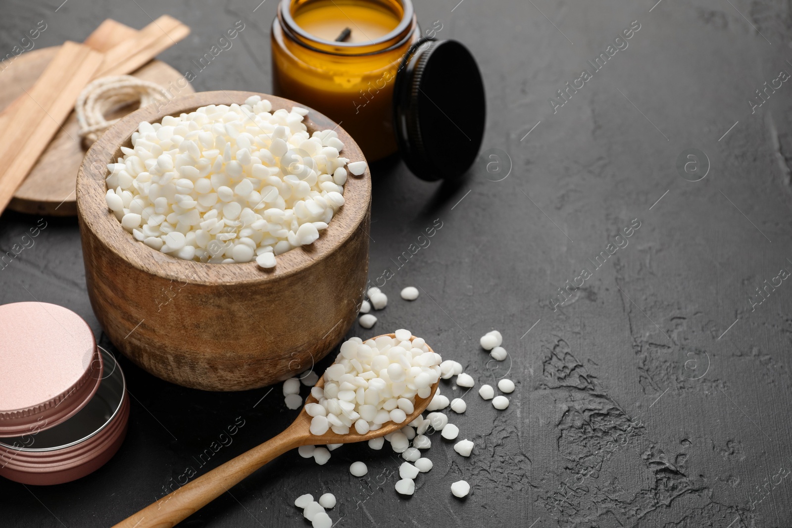 Photo of Soy wax in bowl, candle, wooden wicks and jars on black table, closeup. Space for text