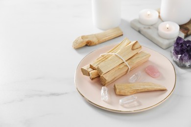 Photo of Palo santo sticks and gemstones on white table. Space for text