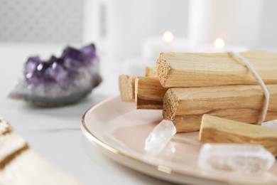 Photo of Palo santo sticks and gemstones on white table, closeup