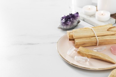 Photo of Palo santo sticks and gemstones on white table. Space for text