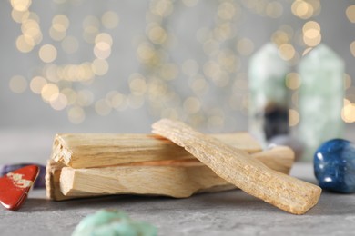 Photo of Palo santo sticks and gemstones on grey table against blurred lights, closeup