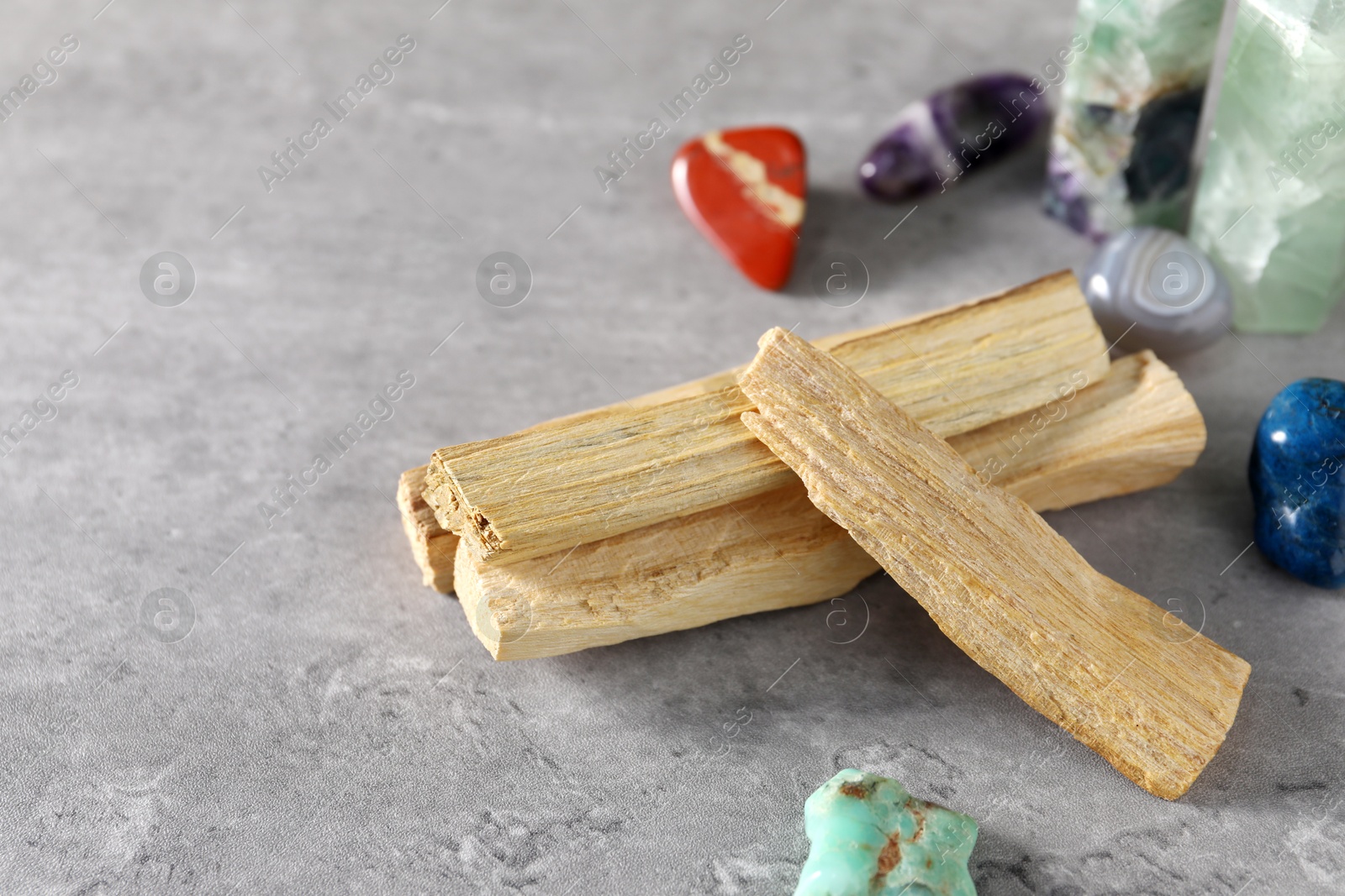 Photo of Palo santo sticks and gemstones on grey table, closeup. Space for text