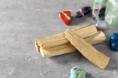 Photo of Palo santo sticks and gemstones on grey table, closeup. Space for text