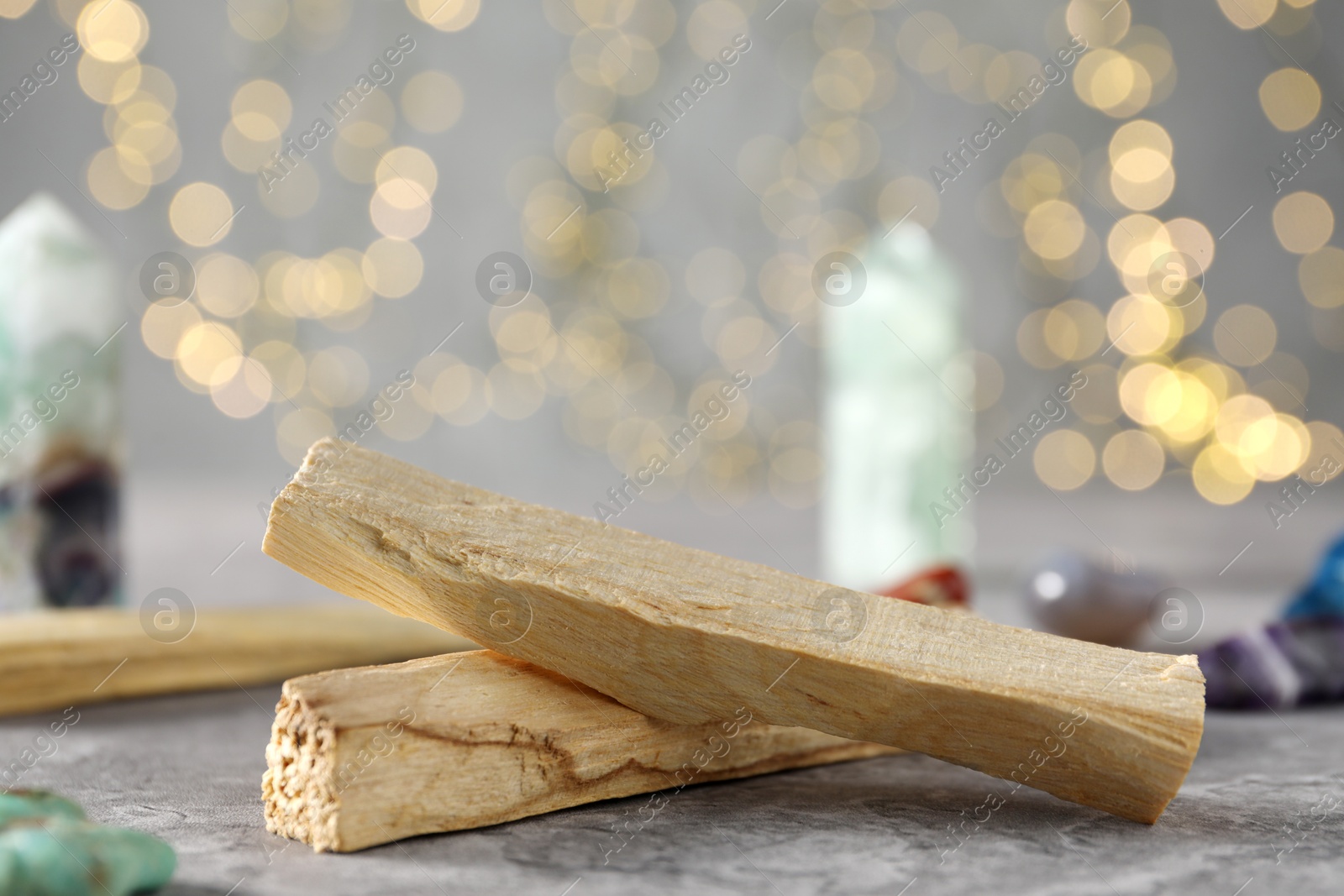 Photo of Palo santo sticks and gemstones on grey table against blurred lights, closeup