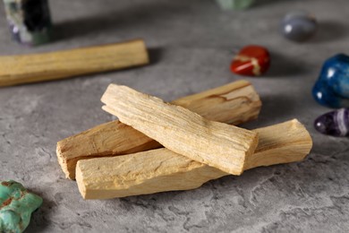 Photo of Palo santo sticks and gemstones on grey table, closeup